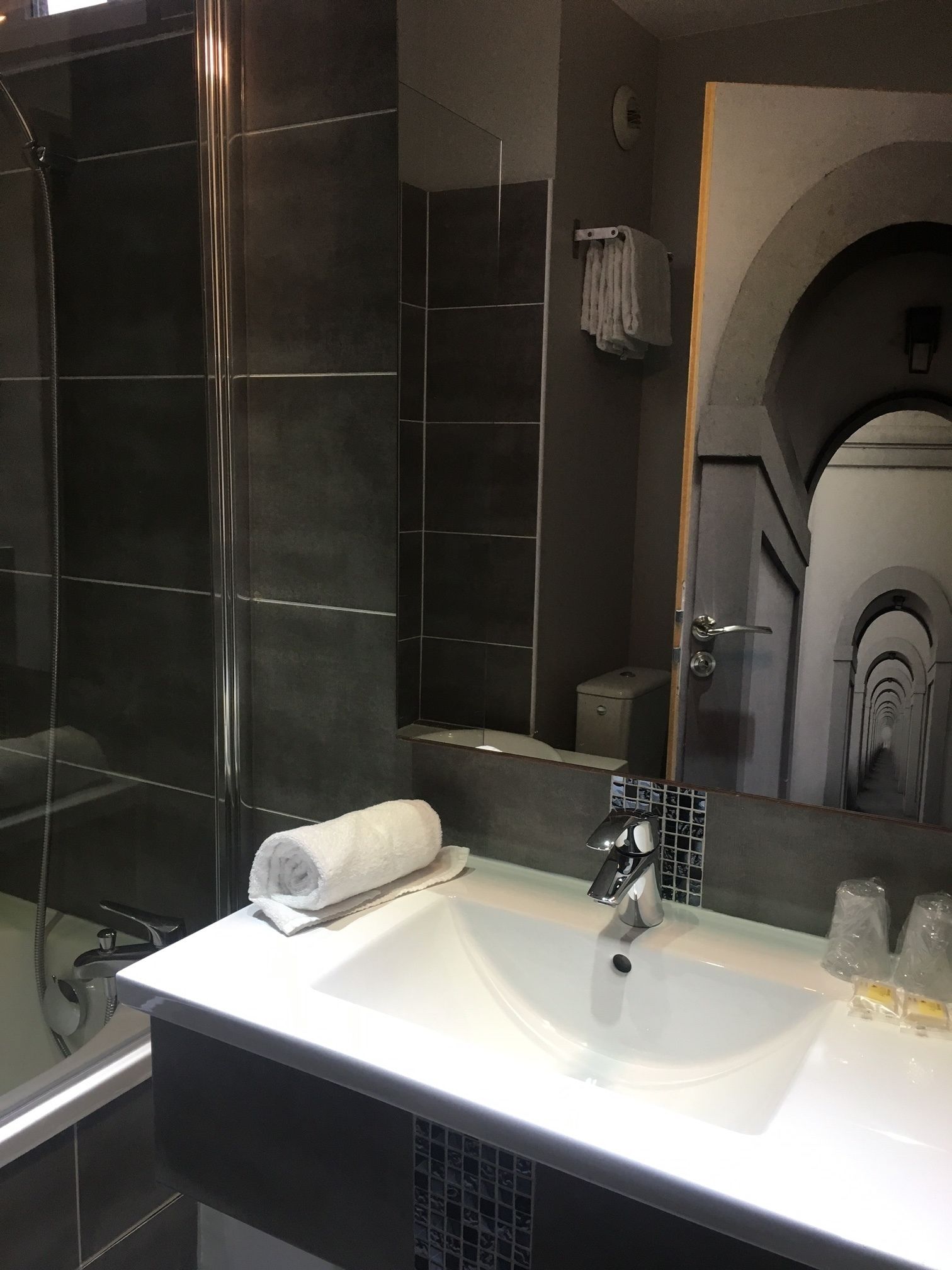 Un baño moderno con cabina de ducha de vidrio, un lavabo blanco y un espejo que refleja un pasillo.
