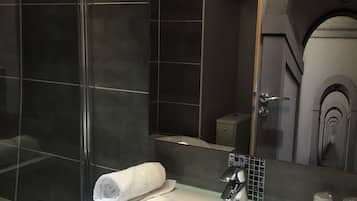 Un baño moderno con cabina de ducha de vidrio, un lavabo blanco y un espejo que refleja un pasillo.