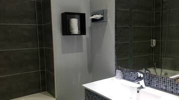 A modern bathroom with dark tiles, a white sink, and a glass shower enclosure.