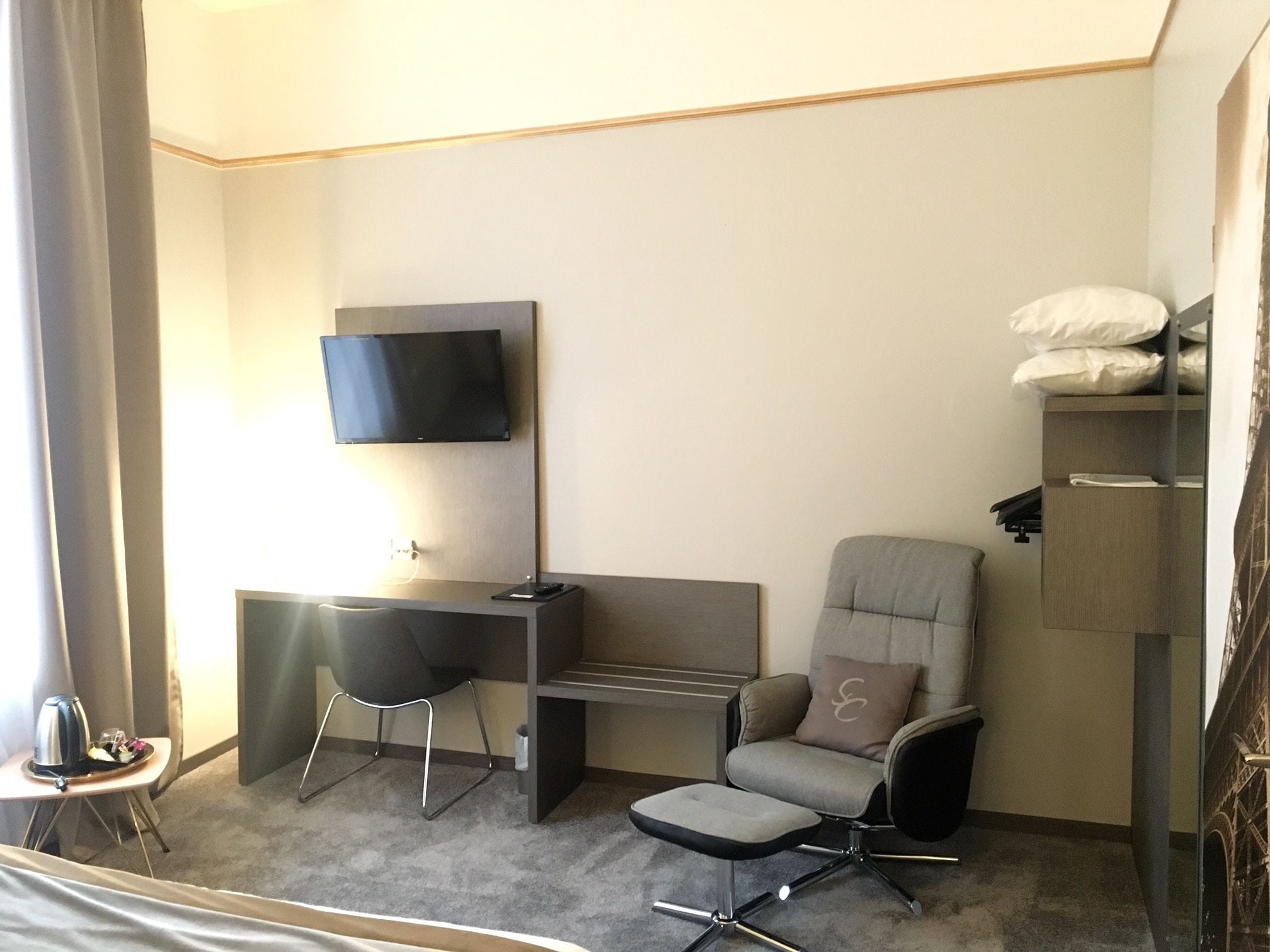 A hotel room with a desk, a chair, a TV, and a bed.