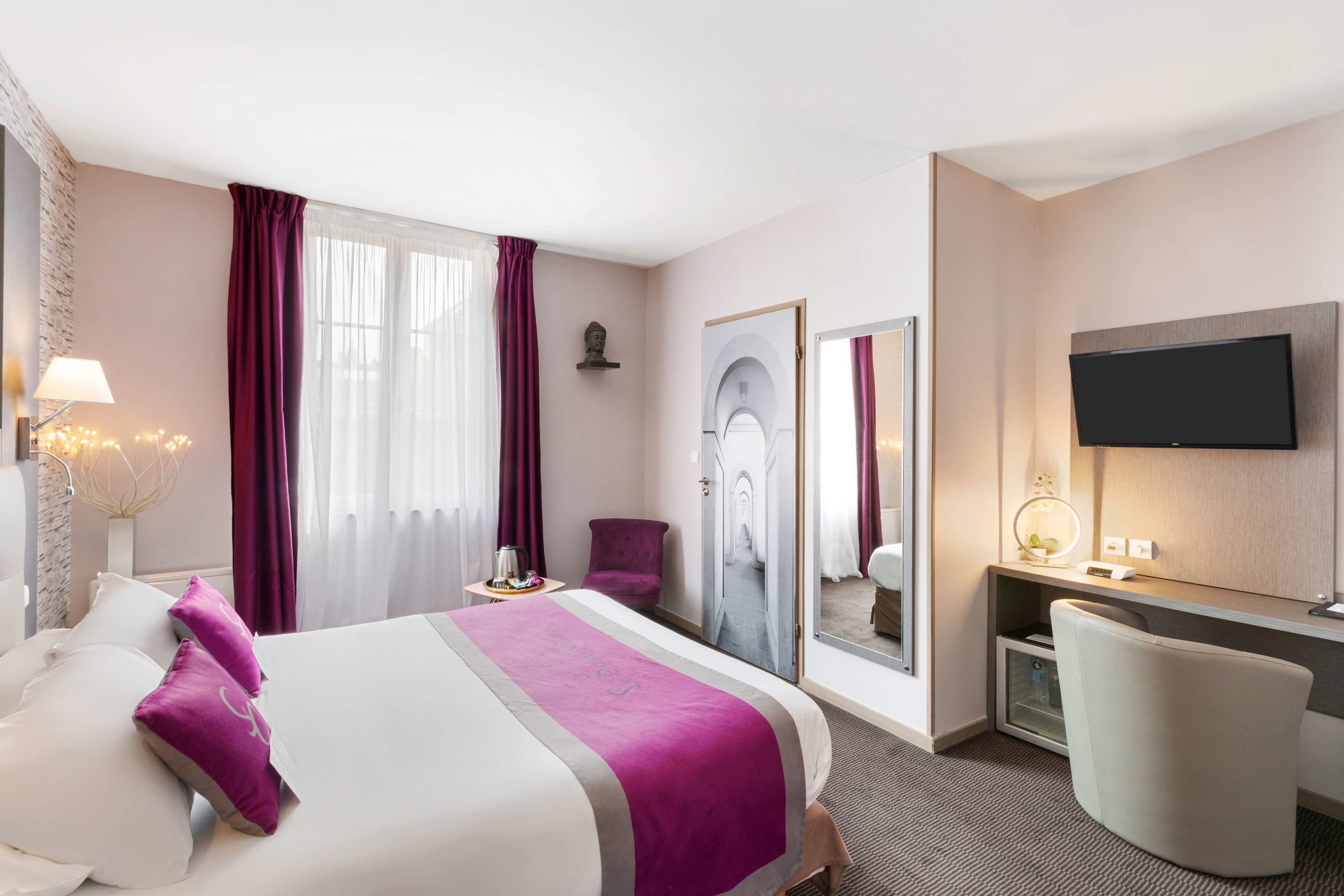 Una habitación de hotel con cama, escritorio, silla, televisor y espejo.