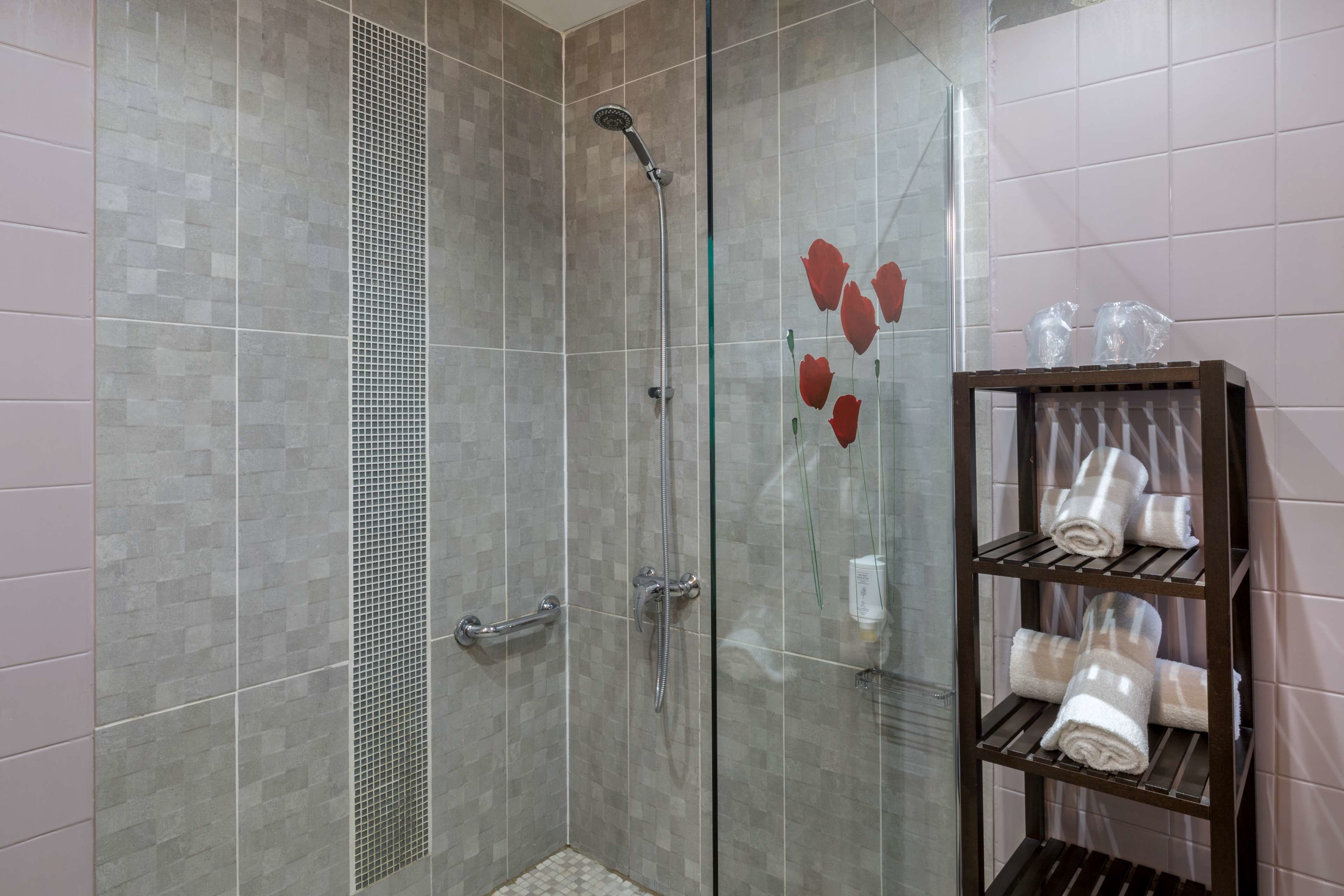 A shower area with a glass door, a metal showerhead, and a shelf with towels.