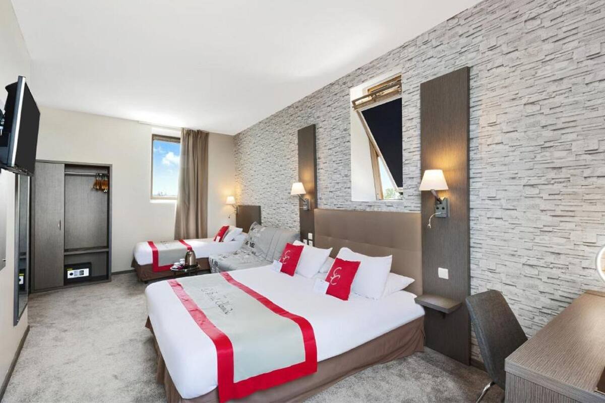 Ein Hotelzimmer mit zwei Betten, einem Schreibtisch, einem Fernseher und einer Wand mit Steinoptik.