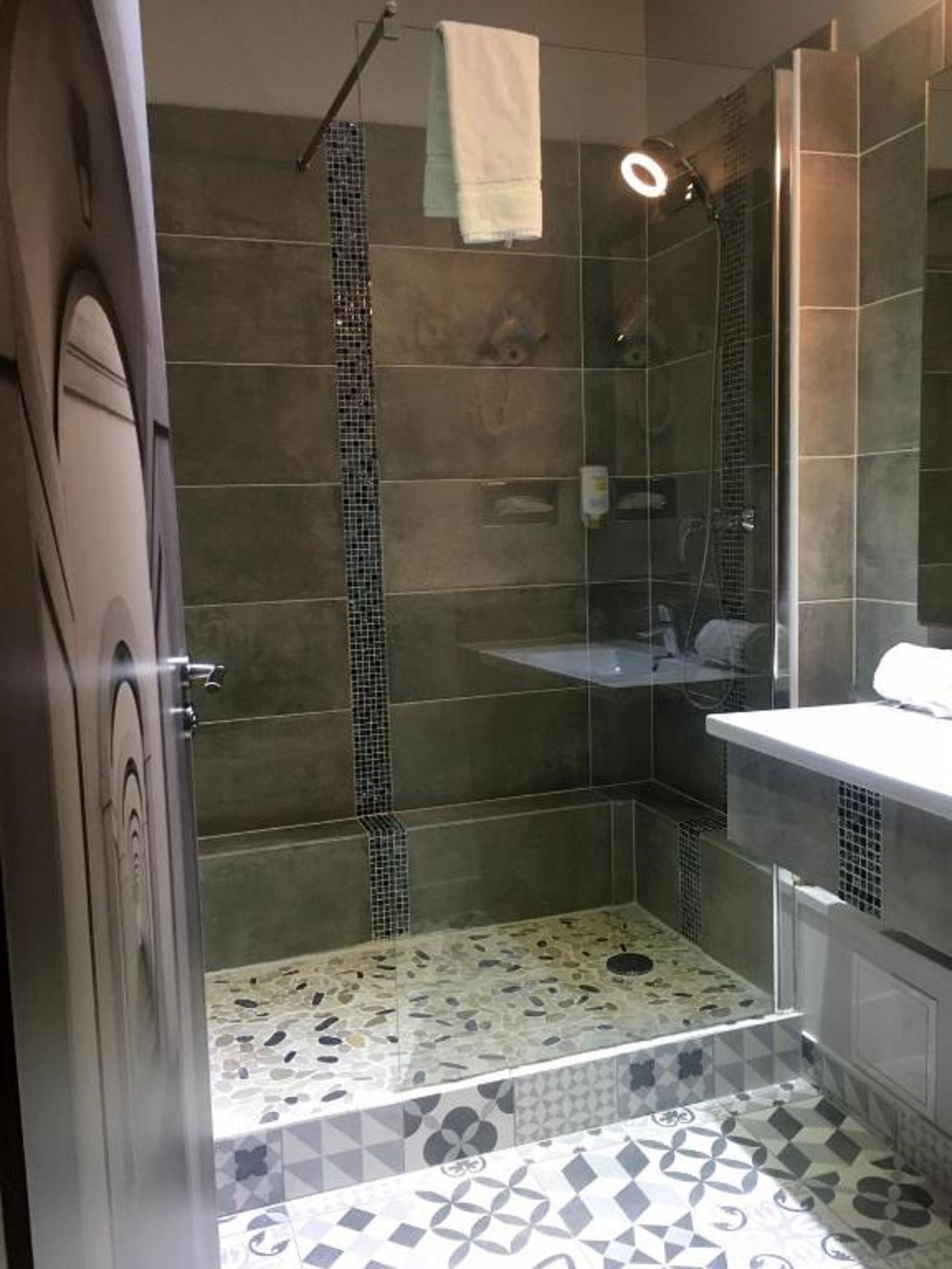 Un baño con ducha, paredes de azulejos, lavamanos e inodoro.