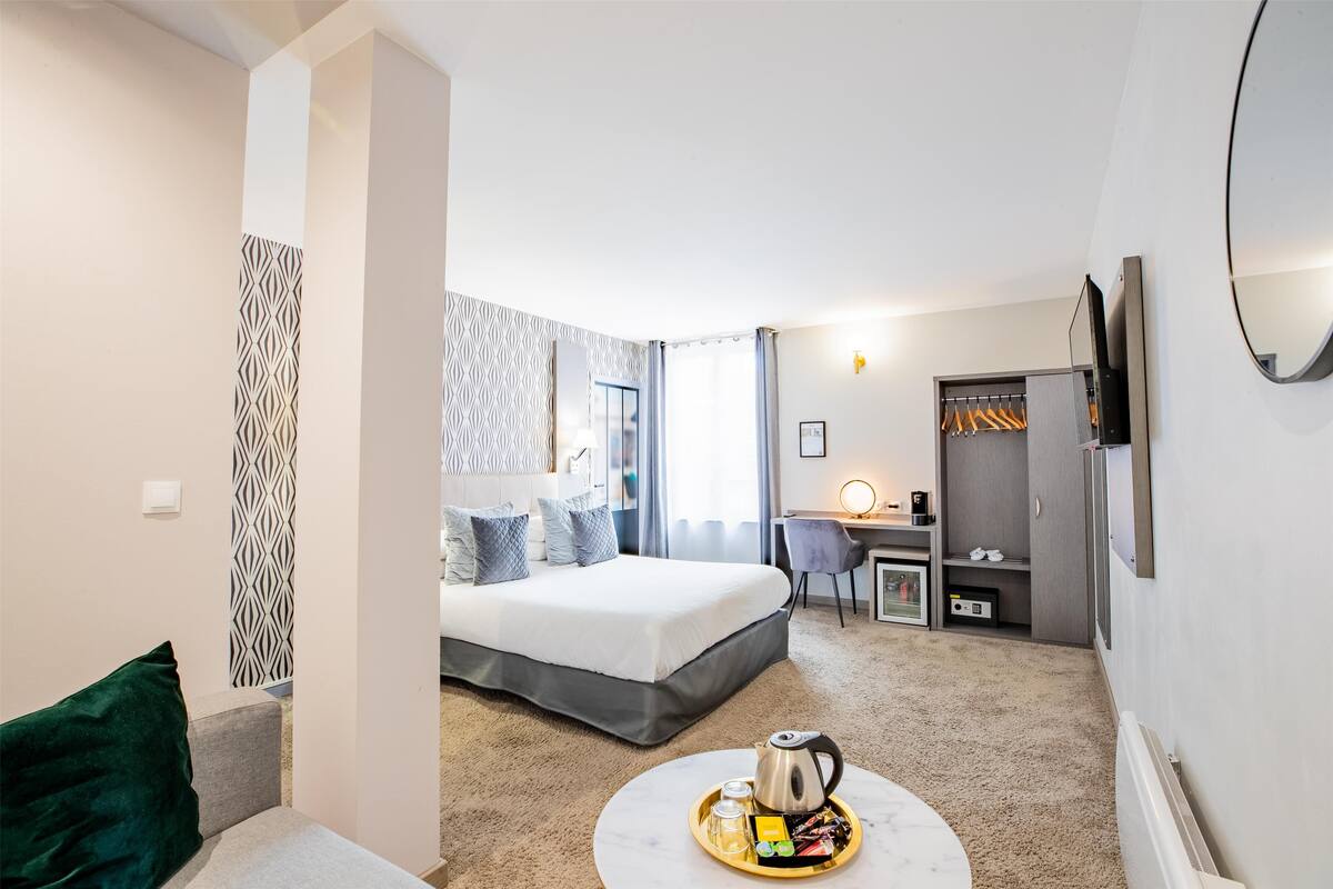 Ein modernes Hotelzimmer mit Bett, Schreibtisch, Kleiderschrank und rundem Couchtisch mit einer Auflage.