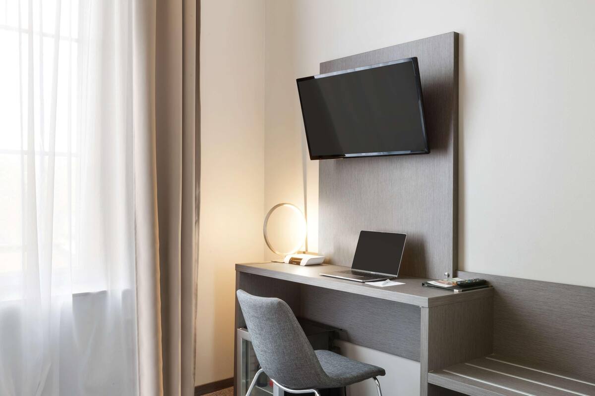 Ein modernes Hotelzimmer mit Schreibtisch, Stuhl, Flachbildfernseher und einer Nachttischlampe.