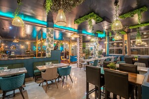 Un restaurante con plantas colgantes verdes, luces colgantes y una zona de bar con mostrador y asientos.