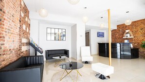 A modern lobby with a brick wall, black leather sofa, white armchair, and a reception desk. - Best Western Hotel Saint Claude (Peronne)