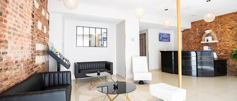 A modern lobby with a brick wall, black leather sofa, white armchair, and a reception desk.