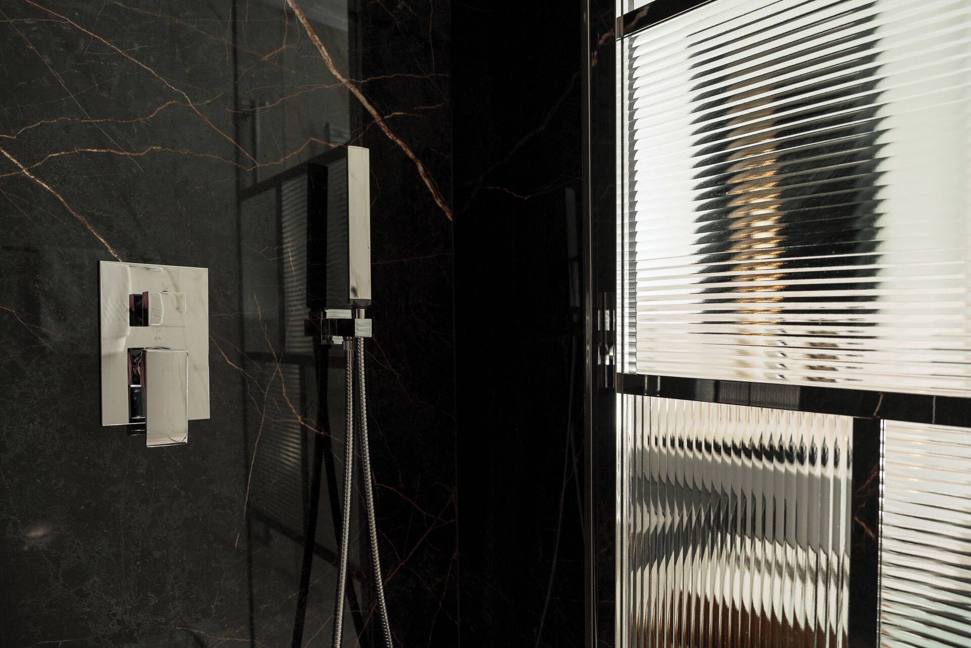 Une salle de bain moderne avec un mur en marbre noir, une douche dotée d’un robinet chromé et une fenêtre avec des stores.