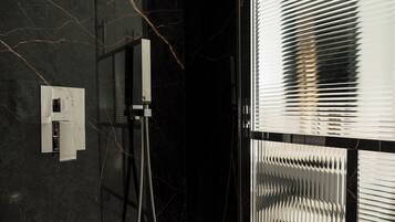 Une salle de bain moderne avec un mur en marbre noir, une douche dotée d’un robinet chromé et une fenêtre avec des stores.