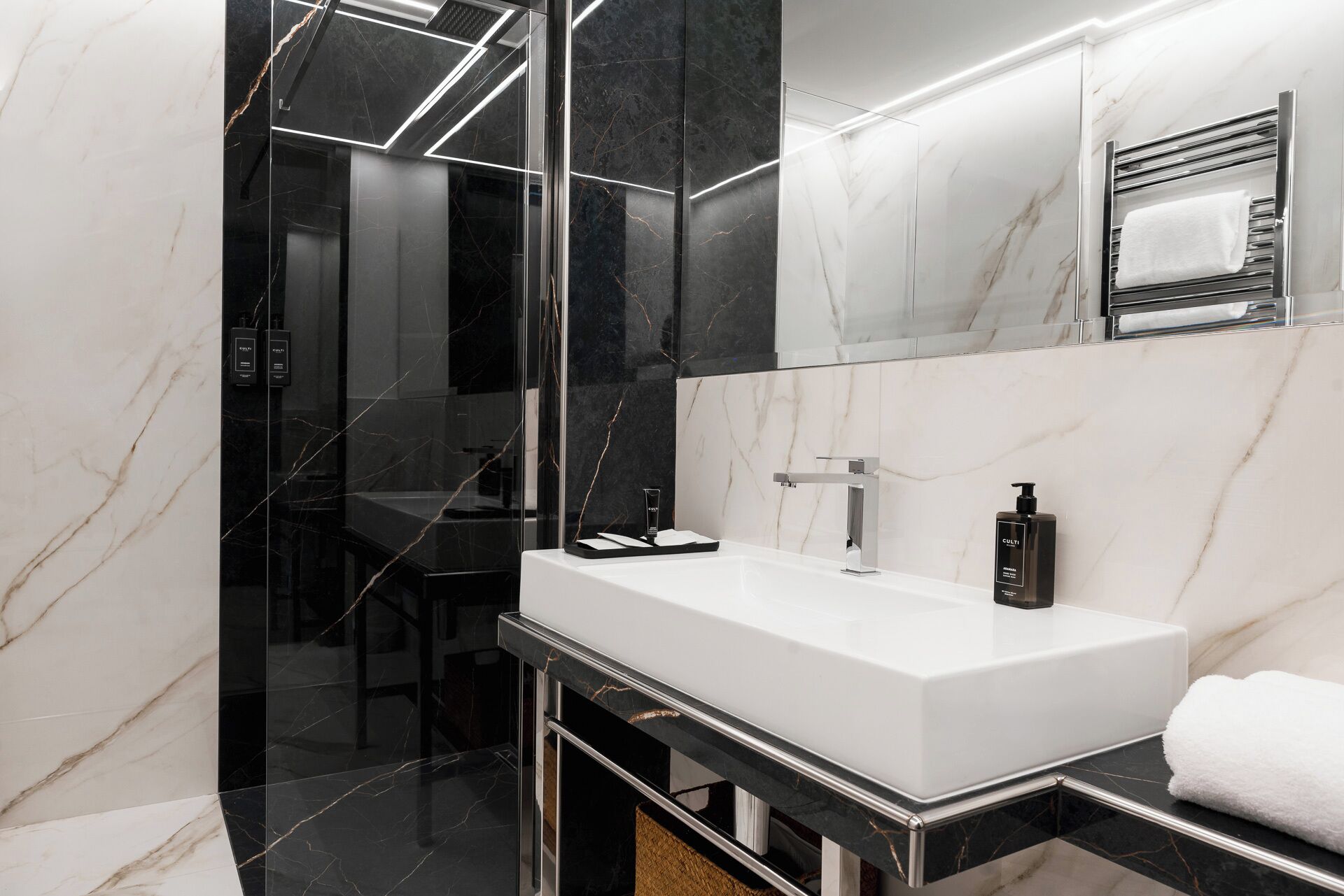 Un bagno moderno con un lavandino bianco, pareti in marmo nero e box doccia in vetro.
