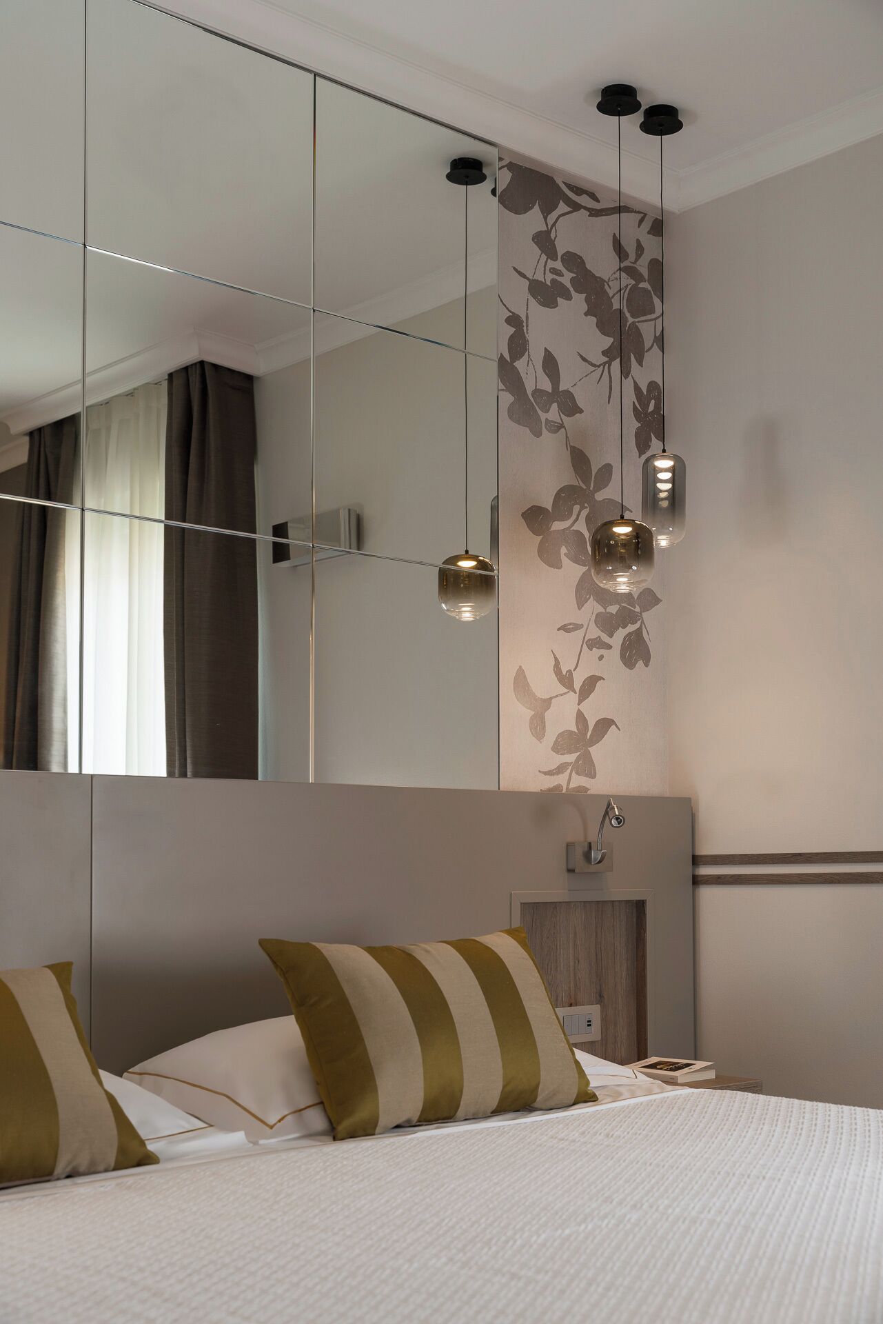 A modern bedroom with a large bed, a mirrored wardrobe, and pendant lights.