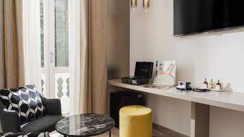 Un soggiorno moderno con un divano, un poggiapiedi giallo rotondo, un tavolino da caffè in vetro, una TV a schermo piatto, un giradischi e una piccola scrivania con un computer e alcuni oggetti sopra.