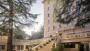 A building with a staircase leading to a balcony, surrounded by potted plants and outdoor seating. - Hotel Helvetia Thermal Spa 4s (Alto Reno Terme)
