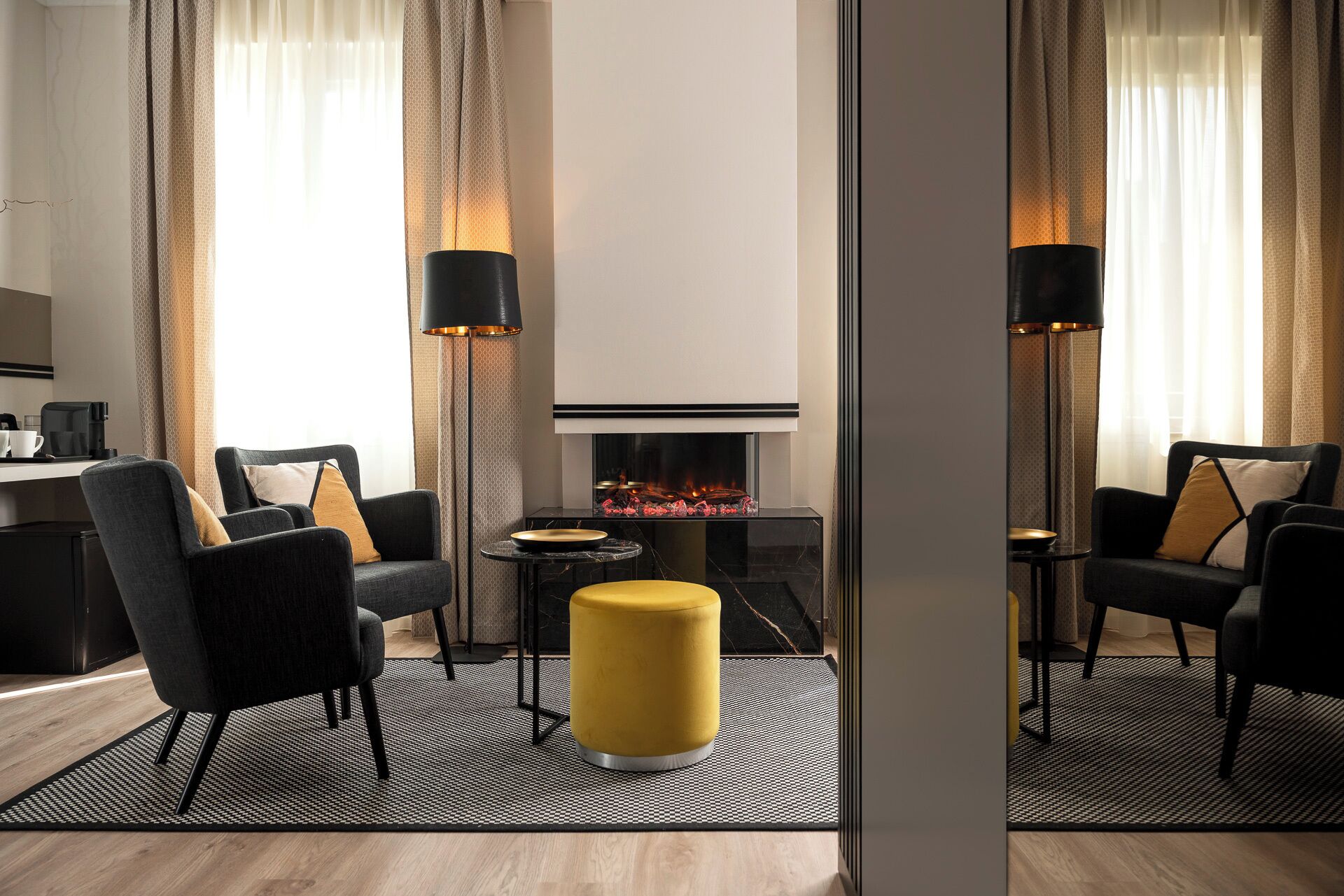 Una habitación de hotel moderna con chimenea, dos sillones, un pouf amarillo y una estación de café.