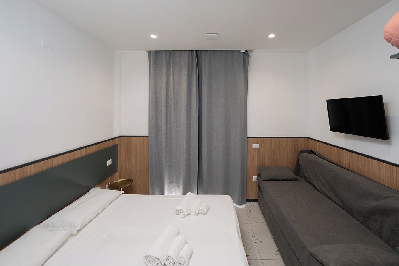 A hotel room with a bed, a sofa, a TV, and a window with curtains.