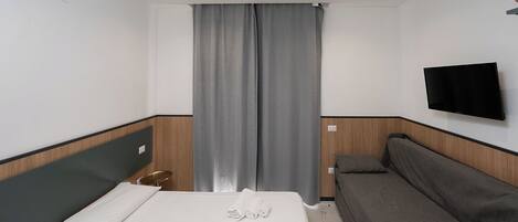 Une chambre d’hôtel avec un lit, un canapé, une télévision et une fenêtre avec des rideaux.