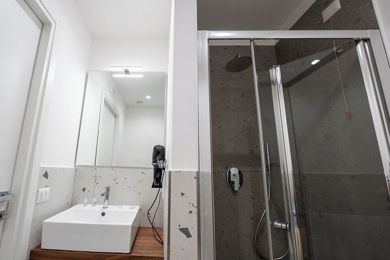 Een moderne badkamer met een witte wastafel, een handdouche en een douchecabine met glazen wanden.