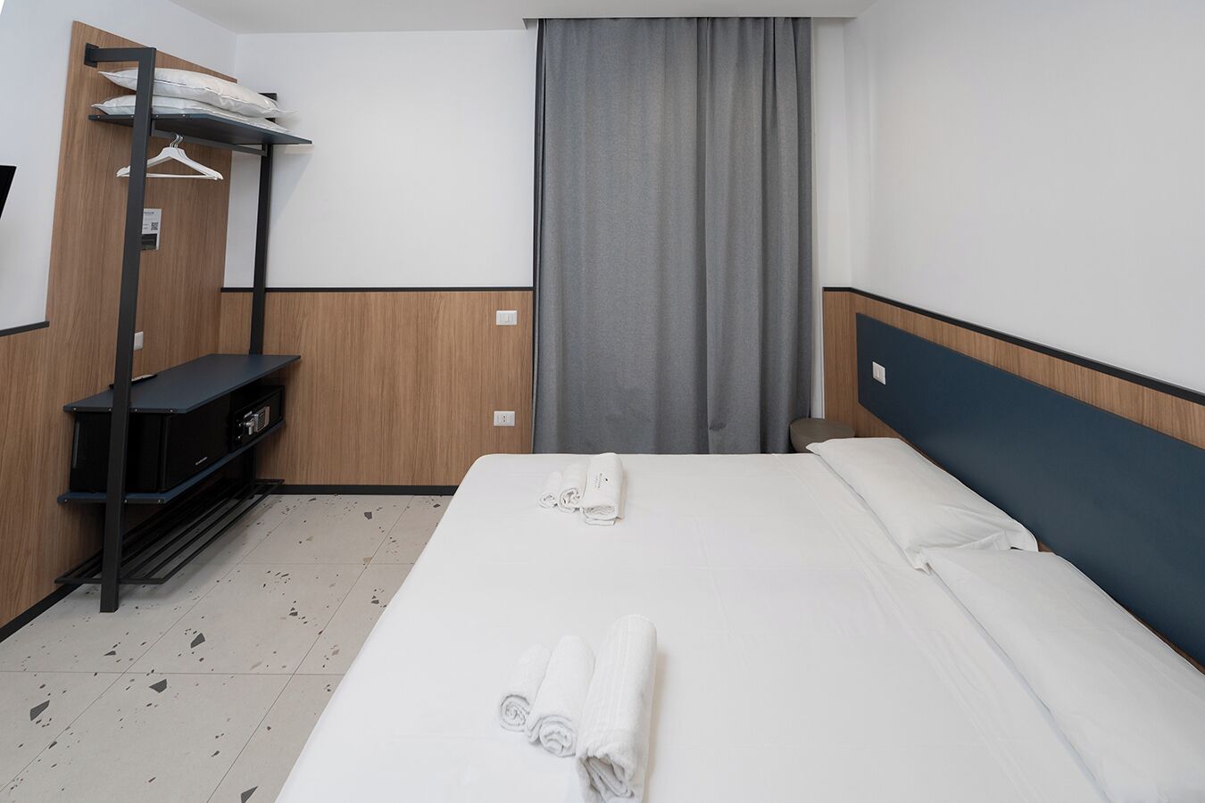 Een hotelkamer met een bed, een kledingkast, een bureau en een raam met gordijnen.