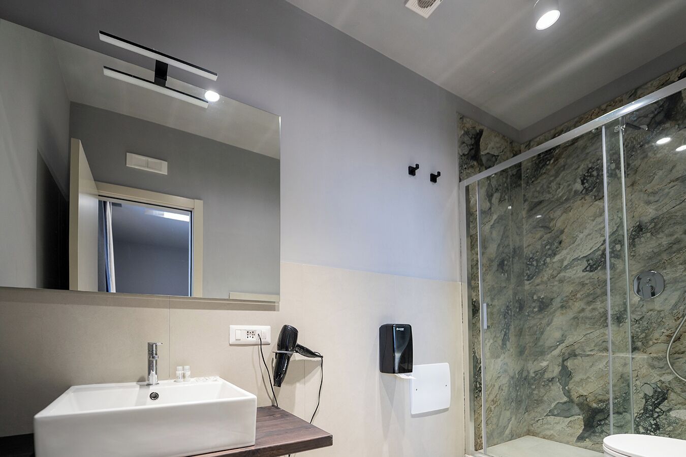 A modern bathroom with a white sink, mirror, and shower with a marble wall.