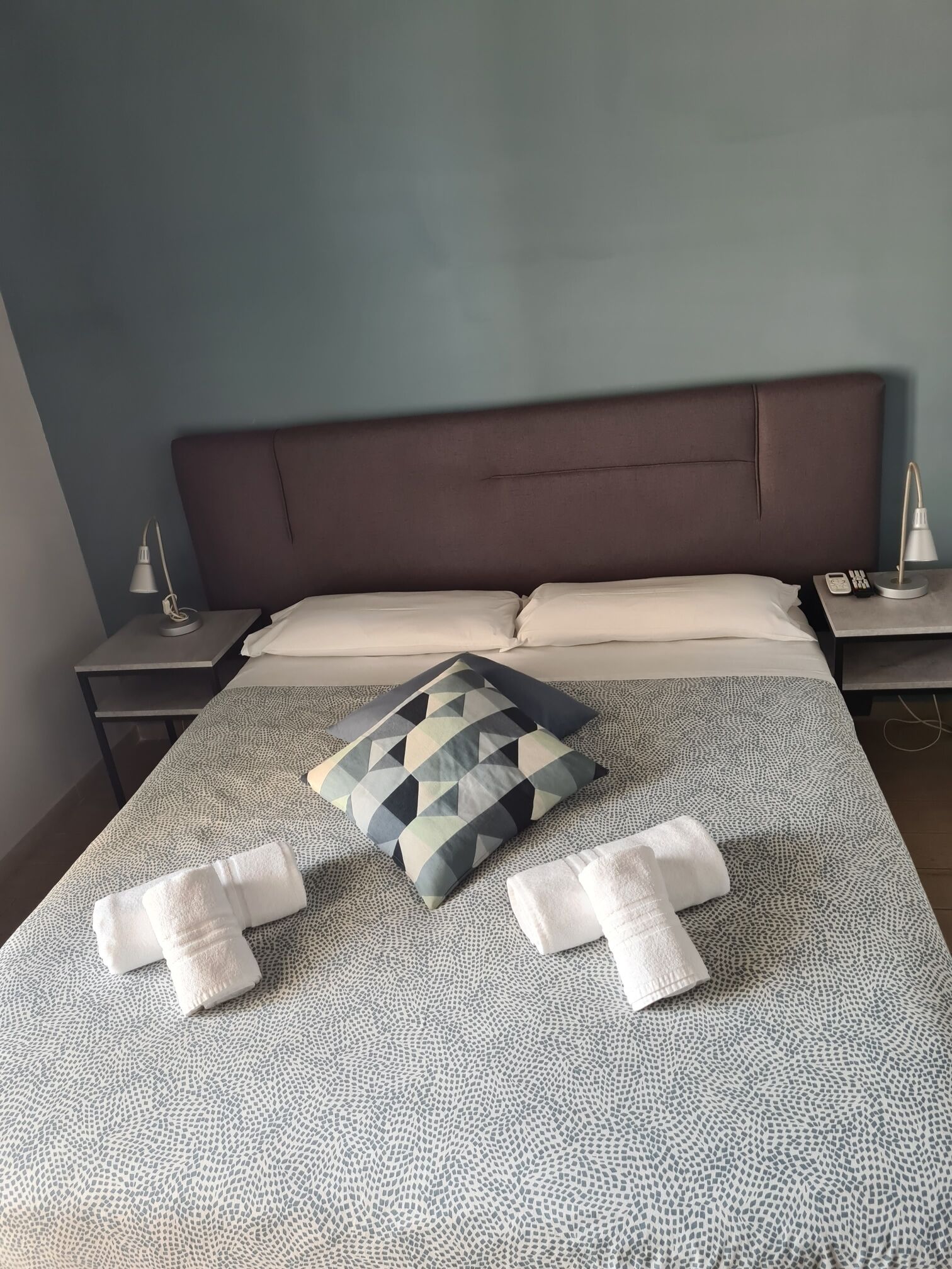 A neatly made bed with a patterned pillow, two bedside tables with lamps, and a blue wall.