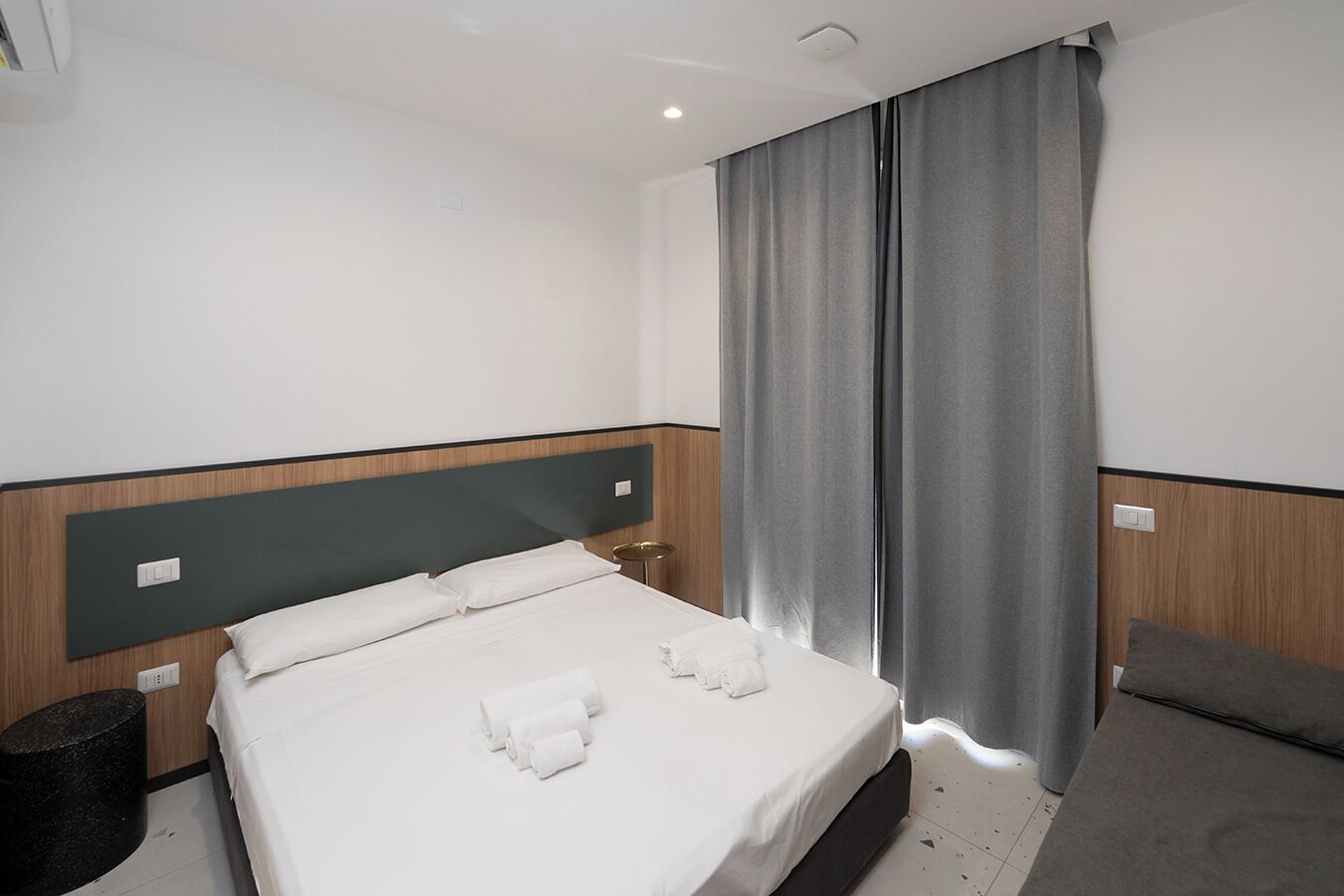 Une chambre d’hôtel avec un lit, une petite table ronde et un rideau gris.