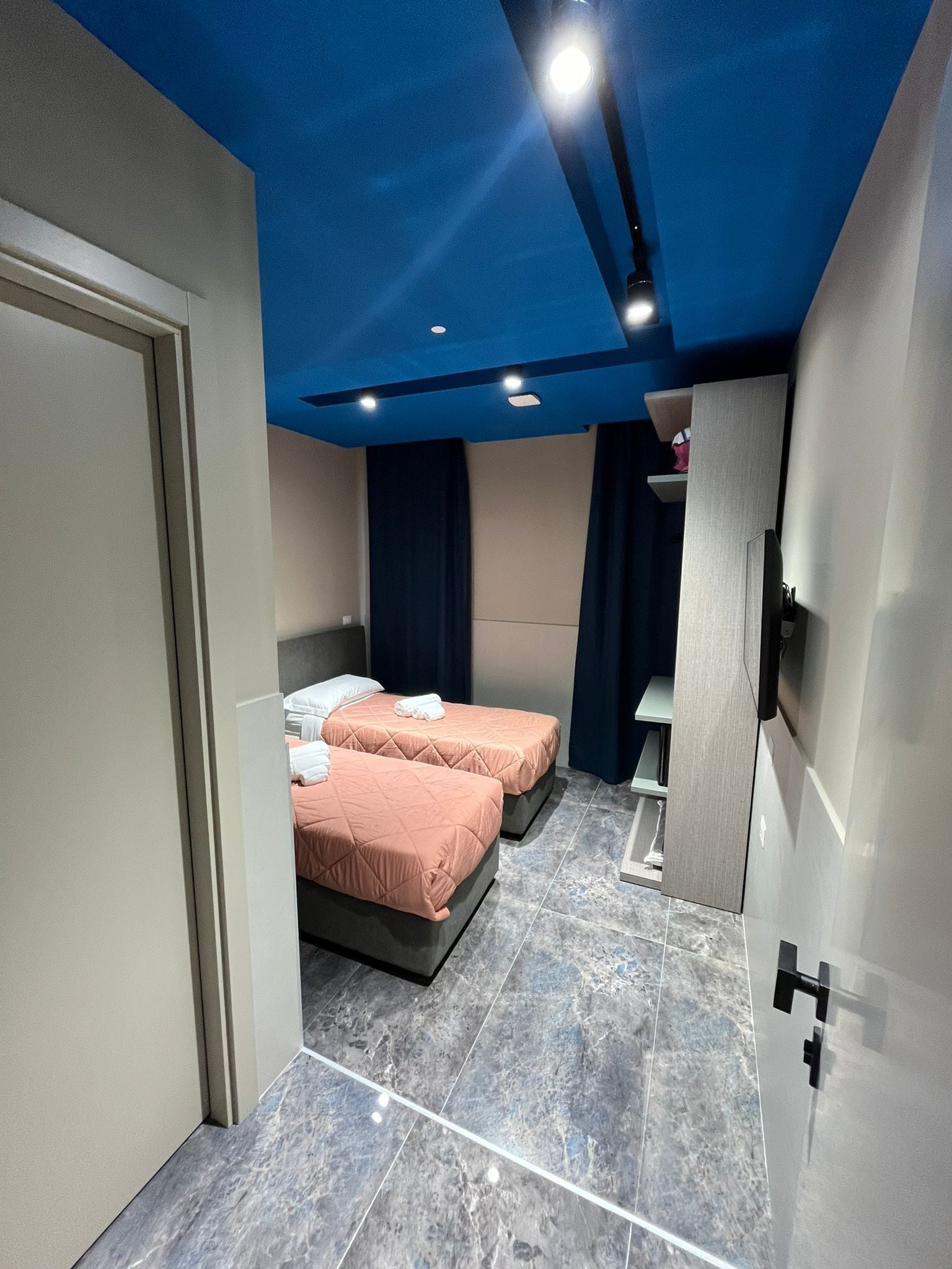 A modern hotel room with two beds, a large mirror, and a wardrobe.