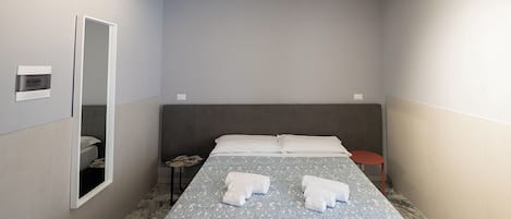 A small, modern hotel room with a single bed, a bedside table, a mirror, and a small red stool.