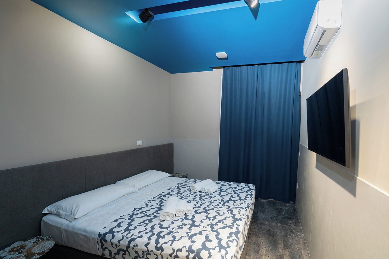 Habitación de hotel con cama, televisor de pantalla plana, aire acondicionado y lámpara en el techo.