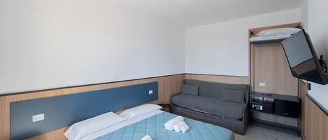 A hotel room with a bed, a sofa, a TV, and a small desk with a computer.