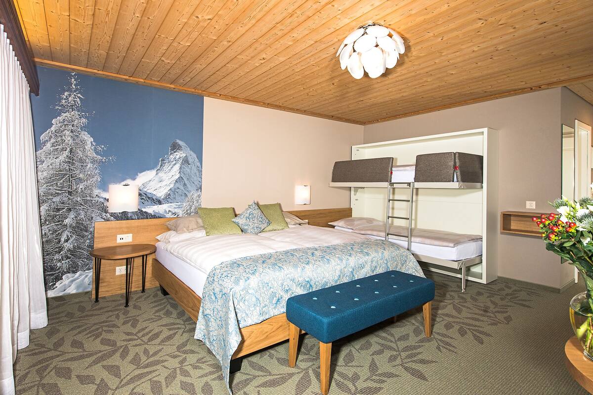 A hotel room with a bed, a bench, a bedside table, a mirror, a wall with a mountain and tree mural, and a ceiling light fixture.