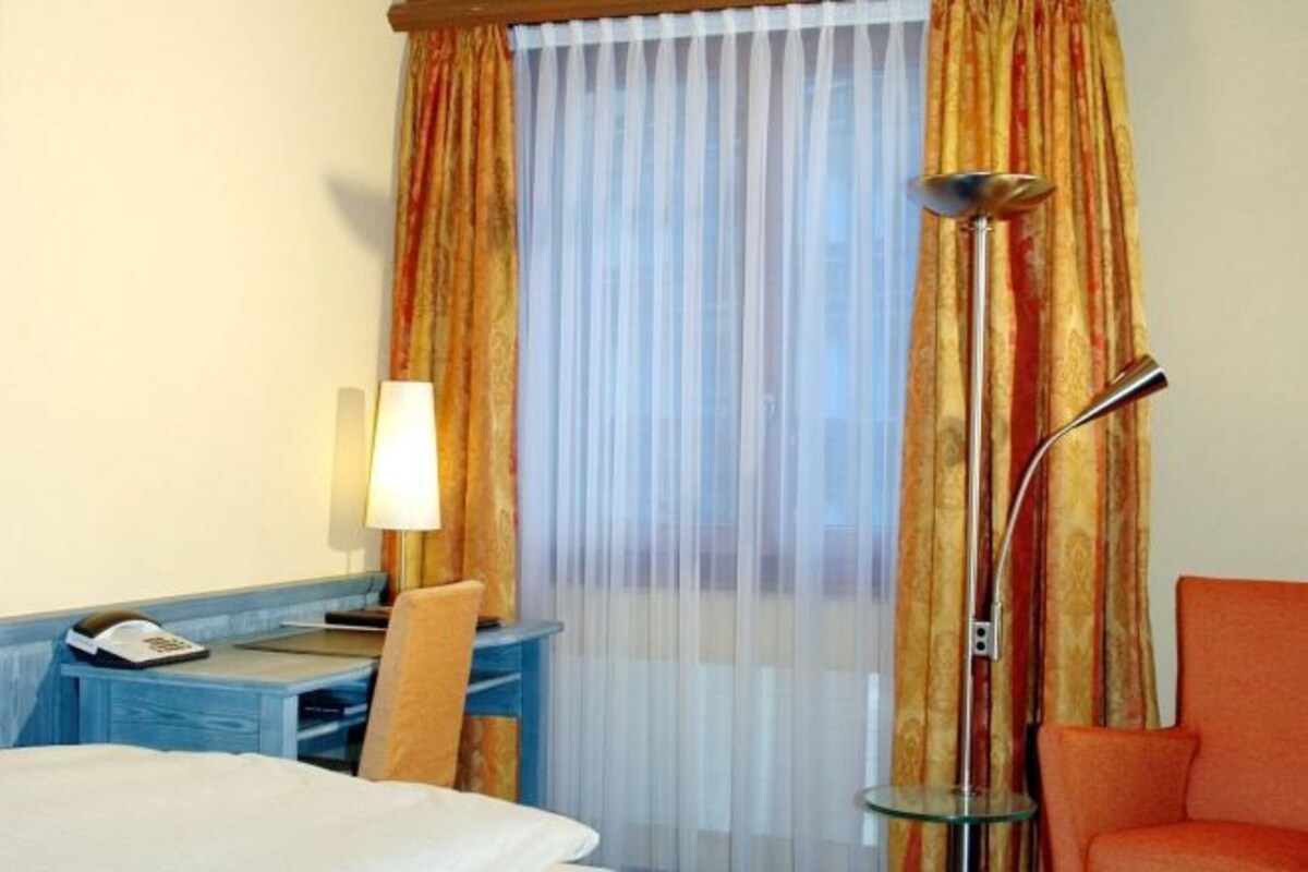 Een hotelkamer met een bed, een bureau met een lamp, een stoel en een vloerlamp.
