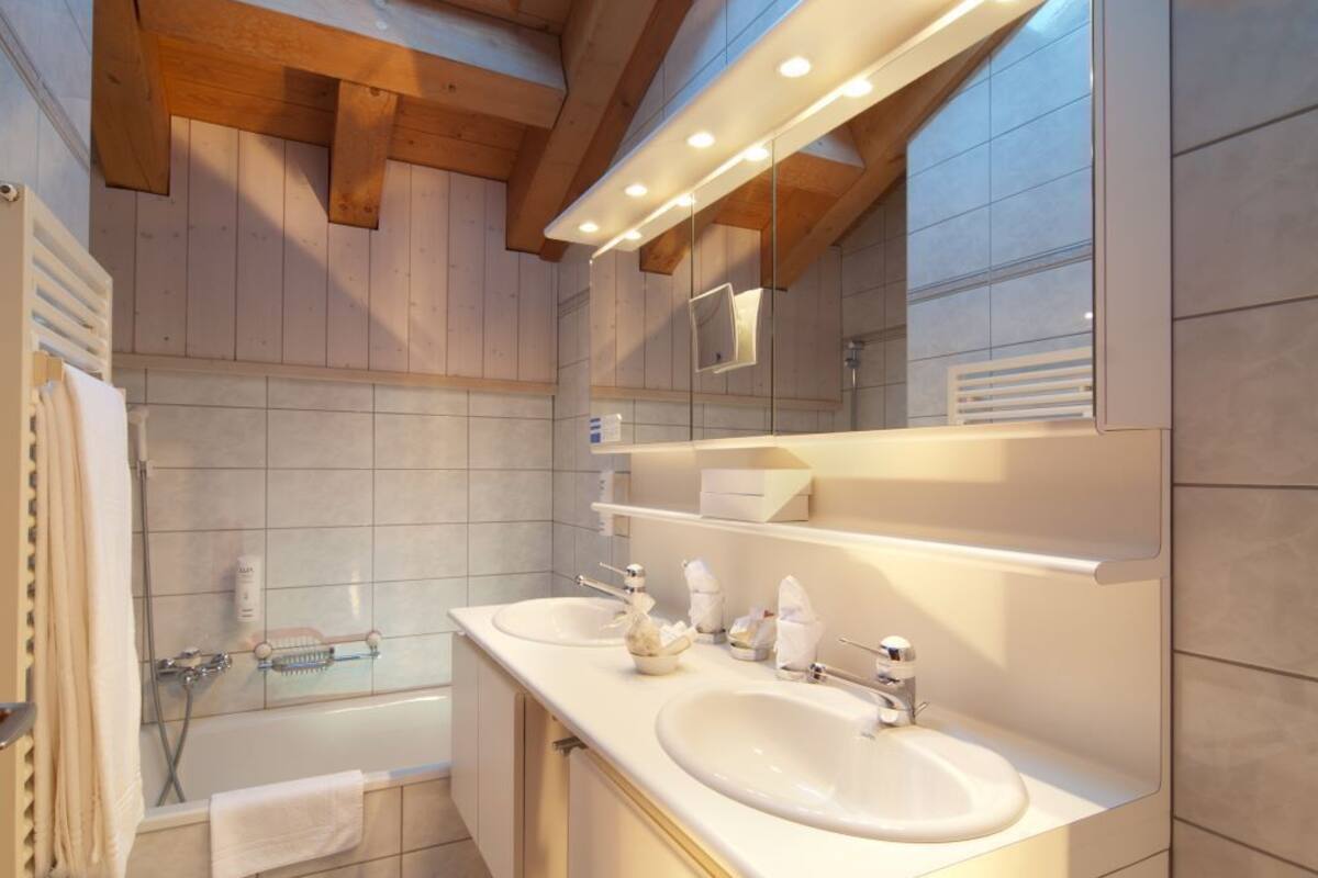 A modern bathroom with two sinks, a large mirror, and wooden beams on the ceiling.