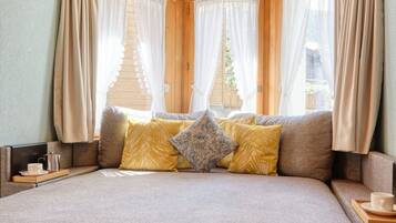 A cozy bedroom with a large bed, wooden ceiling, and windows with curtains.