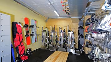 A ski storage room with skis and snowboards on racks, a wooden table, and a storage cabinet.