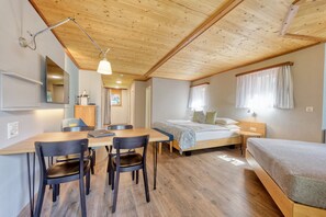A cozy room with a wooden ceiling, a bed with a green bedspread, a desk with chairs, and a small table with a lamp.