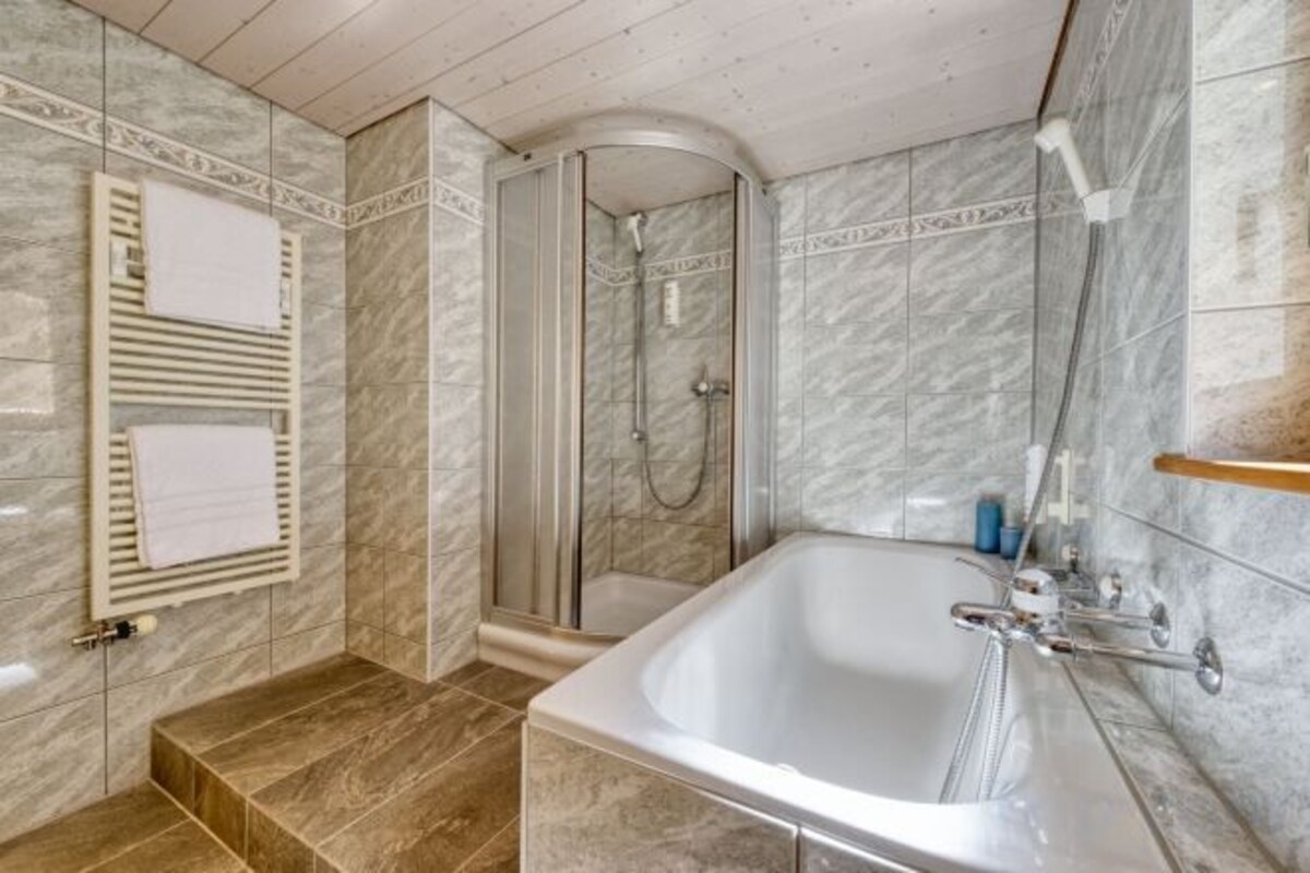 Un baño con bañera, ducha y paredes de azulejos.