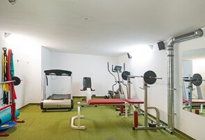 Un gimnasio con varios equipos de ejercicio, incluyendo una cinta de correr, un banco de pesas y pesas sueltas.