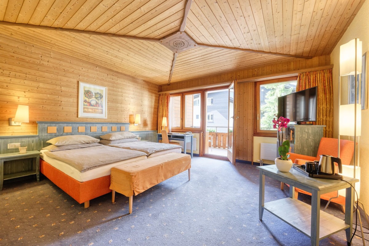 A wooden cabin room with a bed, a desk, a TV, and a window.