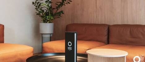 Una habitación de hotel moderna con un sofá de cuero marrón, una pequeña mesa redonda de madera y un dispositivo electrónico negro sobre la mesa.