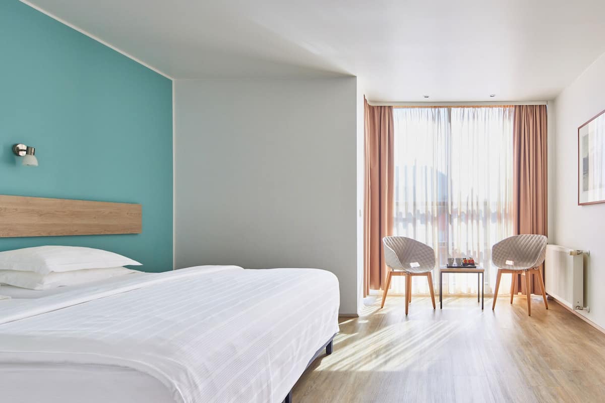 Una habitación de hotel con una cama, una pequeña mesa con sillas y una ventana con cortinas.