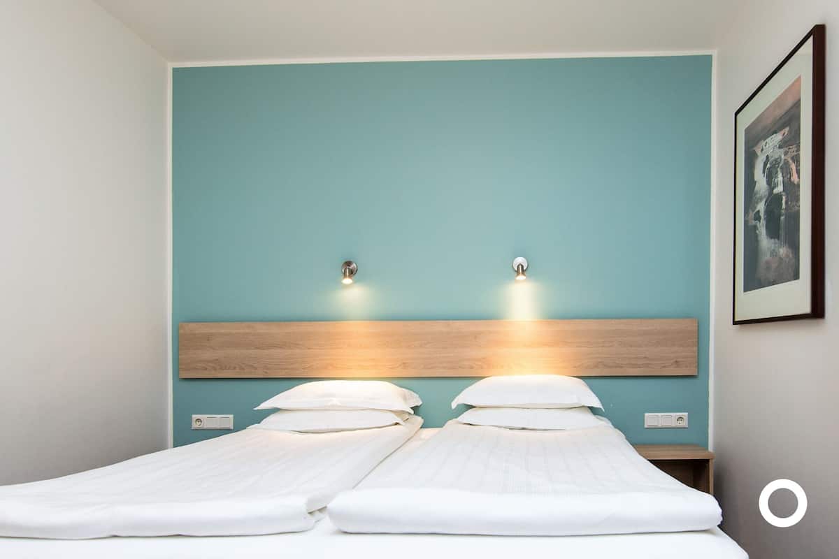 Een tweepersoonsbed met een houten hoofdbord en twee wandlampen.