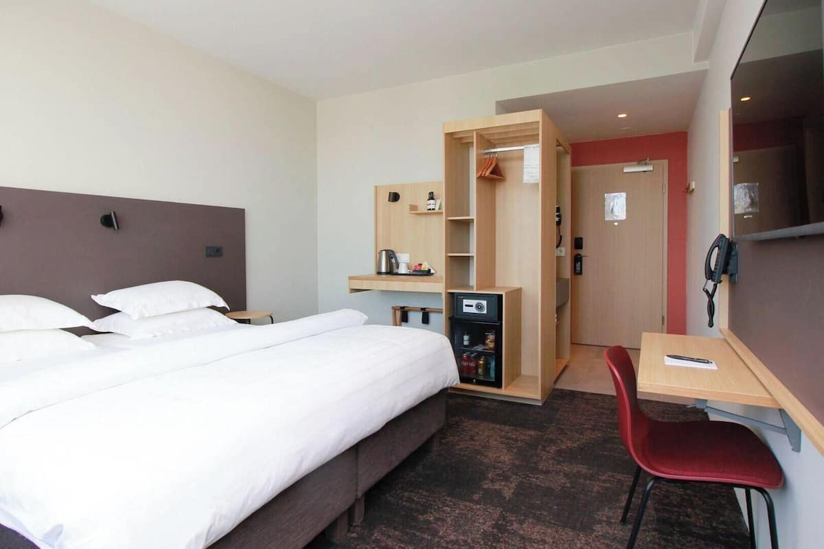 Een hotelkamer met een bed, een bureau, een stoel, een kast en een kleine kitchenette.
