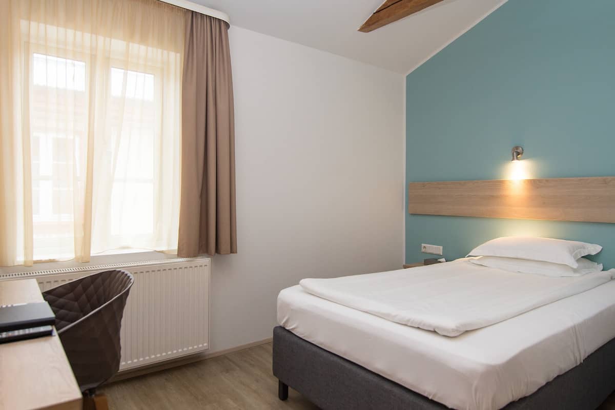 Een hotelkamer met een bed, een bureau, een stoel en een raam met gordijnen.