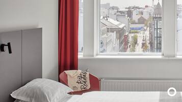 Quarto com cama, cortina vermelha e janela com vista para a cidade.