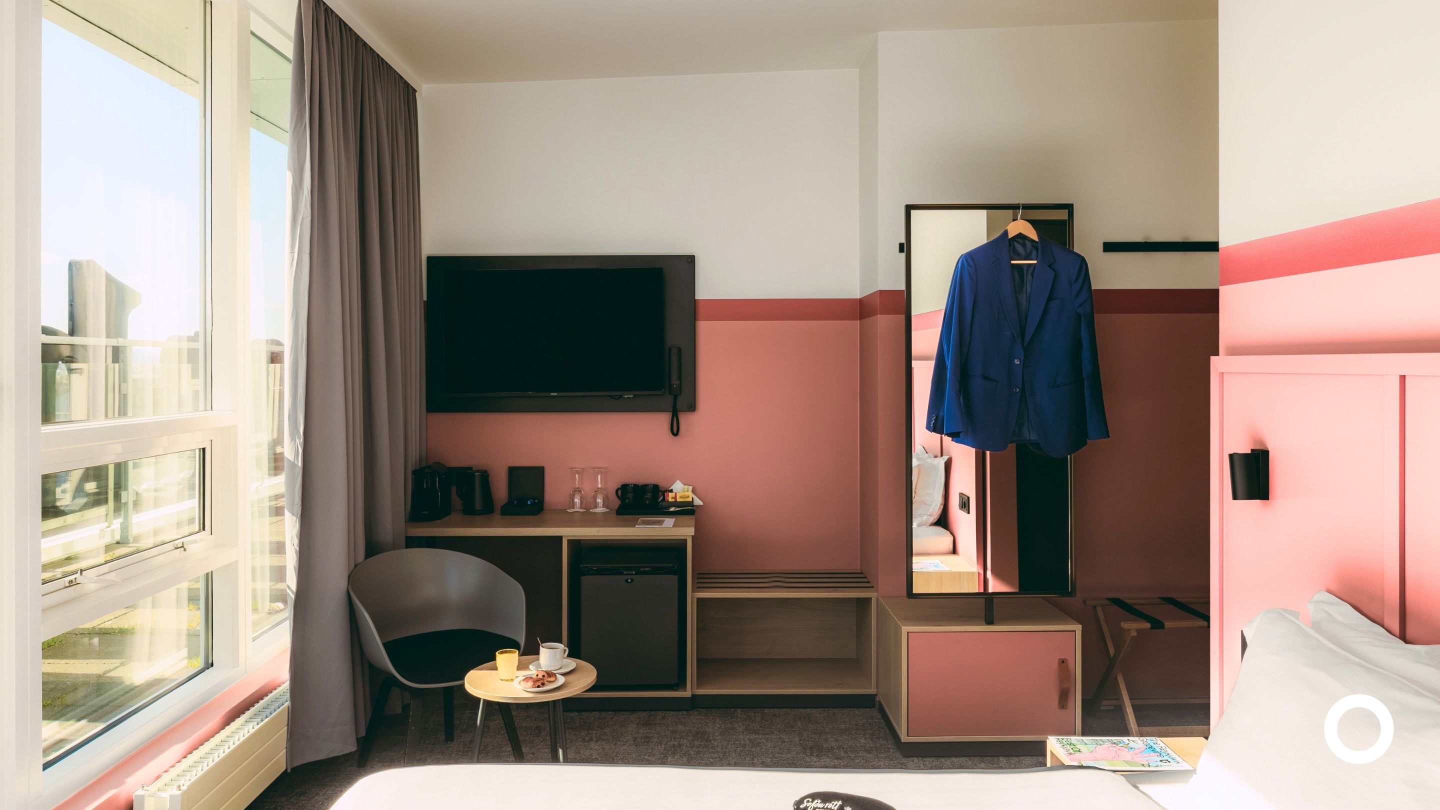 Una habitación de hotel con cama, escritorio con silla, televisor, armario y ventana con cortinas.