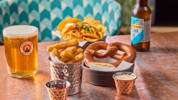 A meal with nachos, pretzel, and fries, a beer glass, and a bottle of beer on a table.