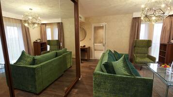 Una habitación con un espejo grande, un sofá verde, un sillón verde y una mesa de centro de vidrio.