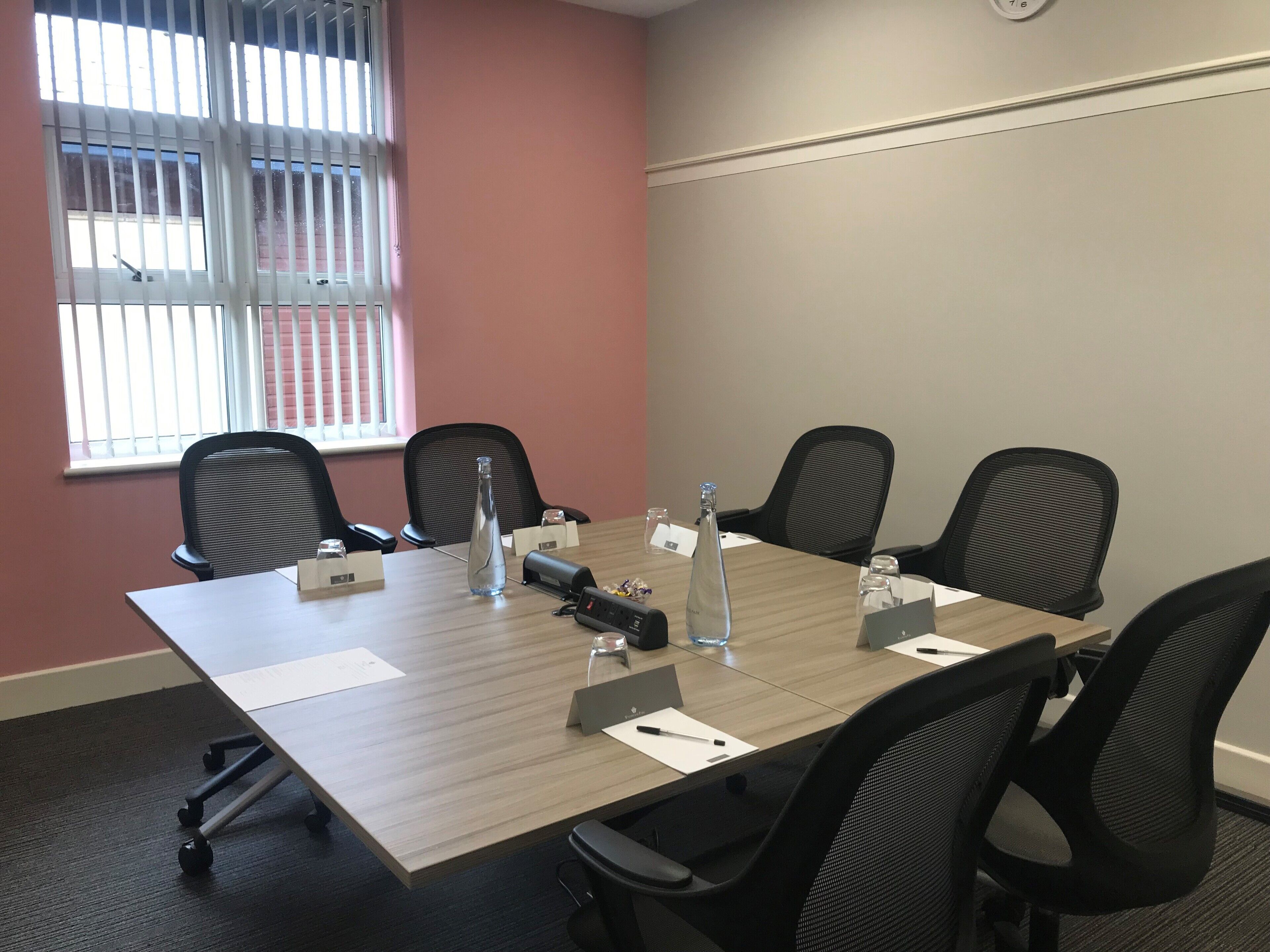 A conference room with a long table, four chairs, nameplates, water bottles, and a projector.
